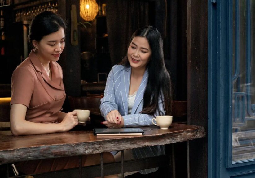 Two women sitting at a bar with coffee and tablet.